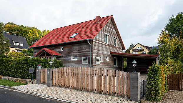 Holzhaus mit Satteldach Holzhaus mit rotem Satteldach und Naturzaun im Wohngebiet