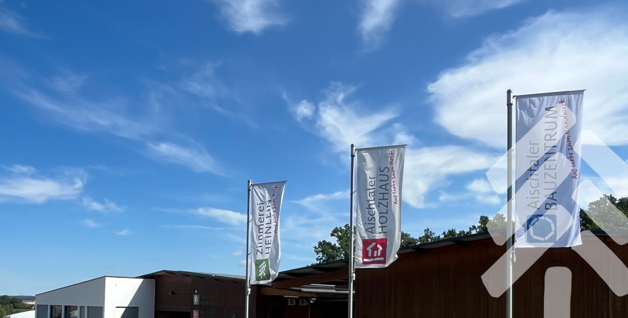 Firmengebäude mit Fahnen von Zimmerei Heinlein, Aischtaler Holzhaus und Aischtaler Bauzentrum in Neustadt an der Aisch