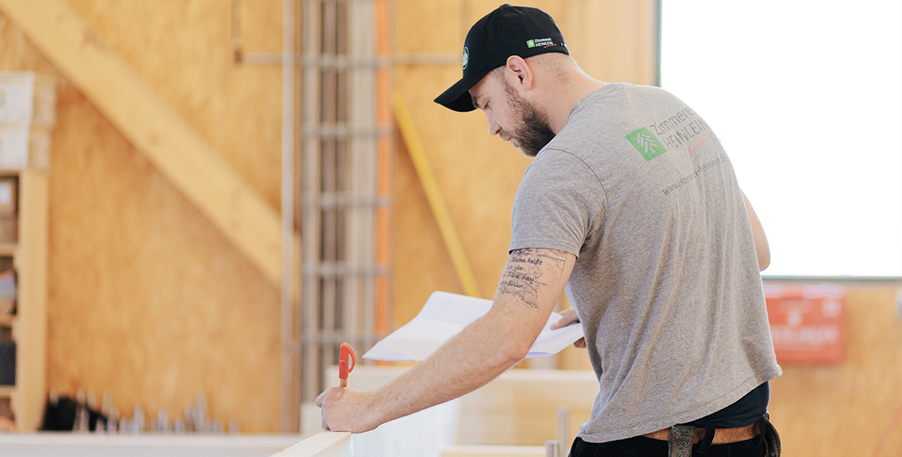 Zimmerer prüft Baupläne in der Holzwerkstatt – präzise Planung im Holzbau