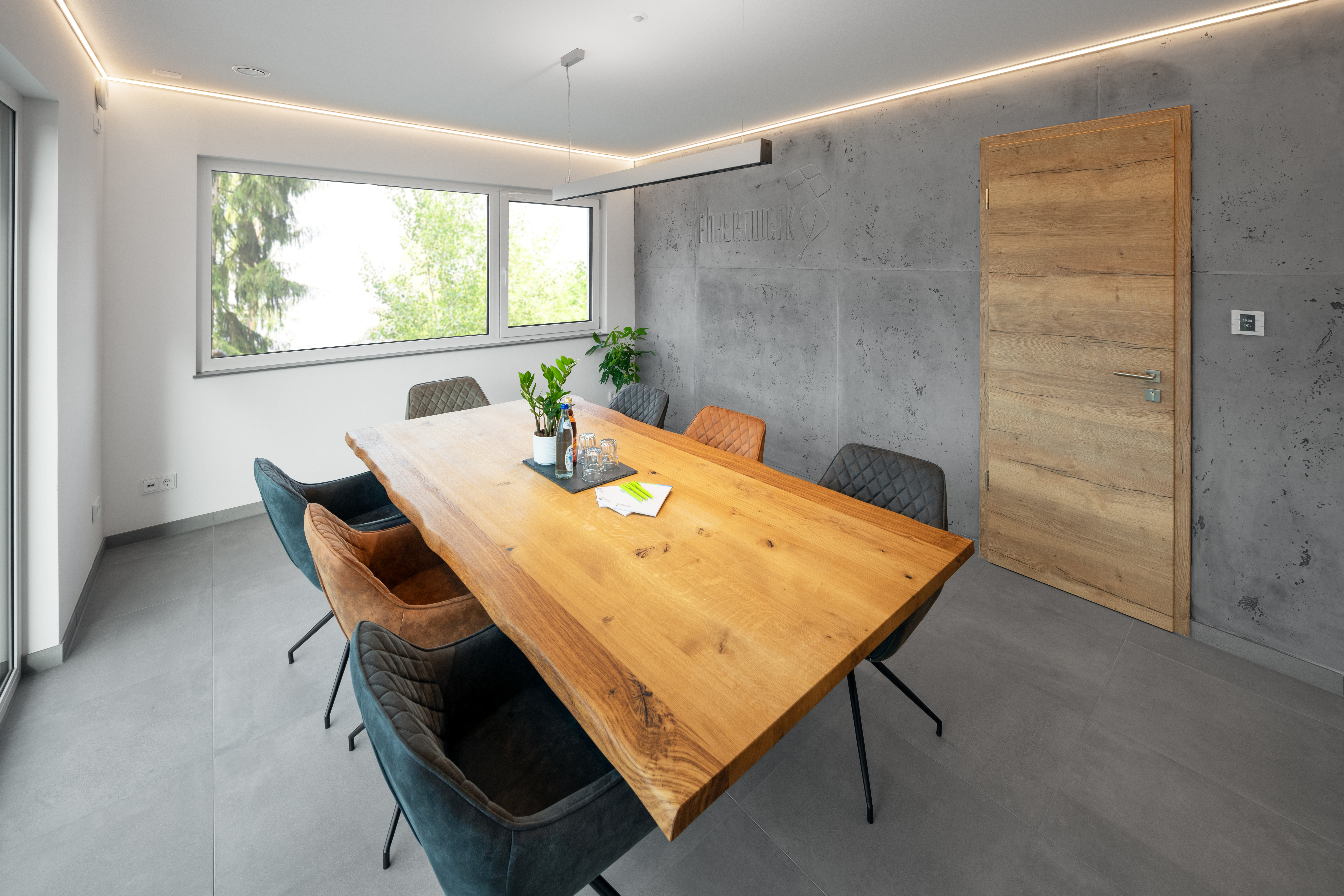 Besprechungsraum im "Phasenwerk", Naturholztisch mit schwarz und braunen Lederstühlen vor einer Betonwand 