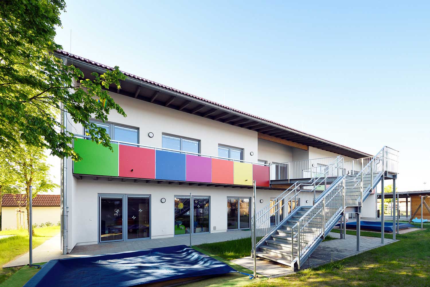 Außenbereich der "Schatzkiste" mit abgedecktem Sandkasten, buntem Balkon und Edelstahltreppe