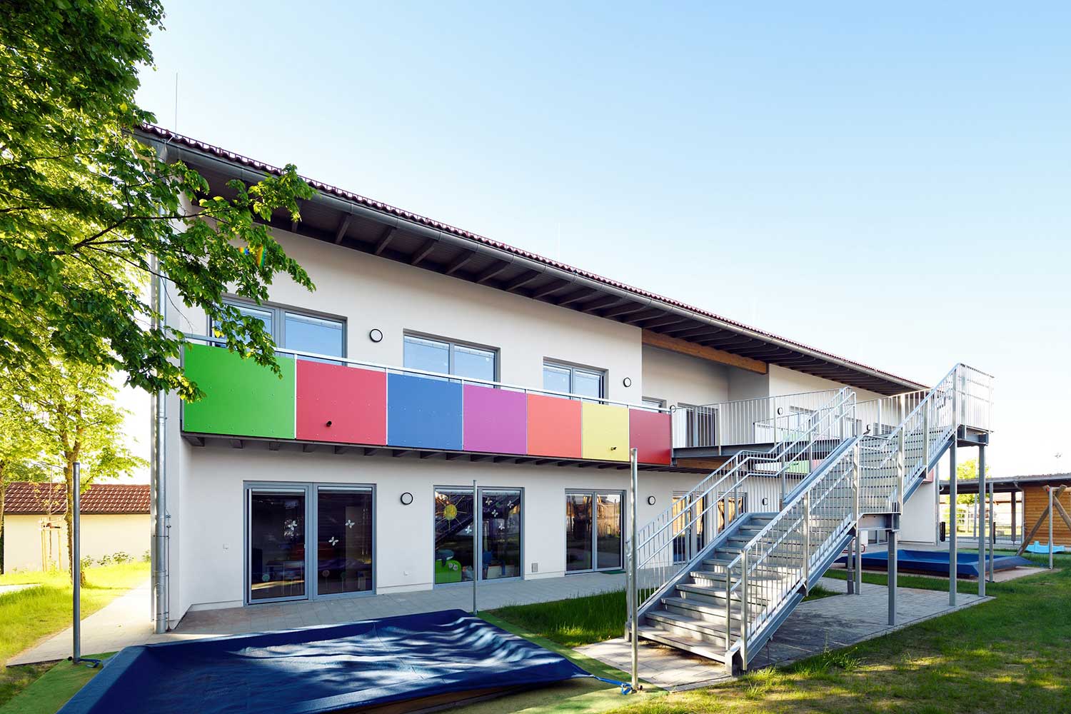 Außenbereich der "Schatzkiste" mit abgedecktem Sandkasten, buntem Balkon und Edelstahltreppe