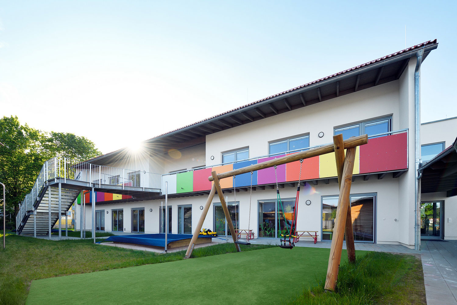 Außenbereich der Kindertagesstätte Schatzkiste mit Sandkasten, buntem Balkon und einer Holzschaukel