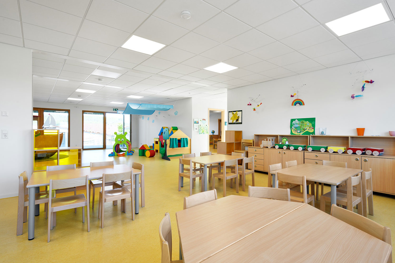 Gruppenraum der Kindertagesstätte "Schatzkiste" mit Stühlen und Tischen für Kinder im hinteren Teil des Raums ist ein Spielbereich 