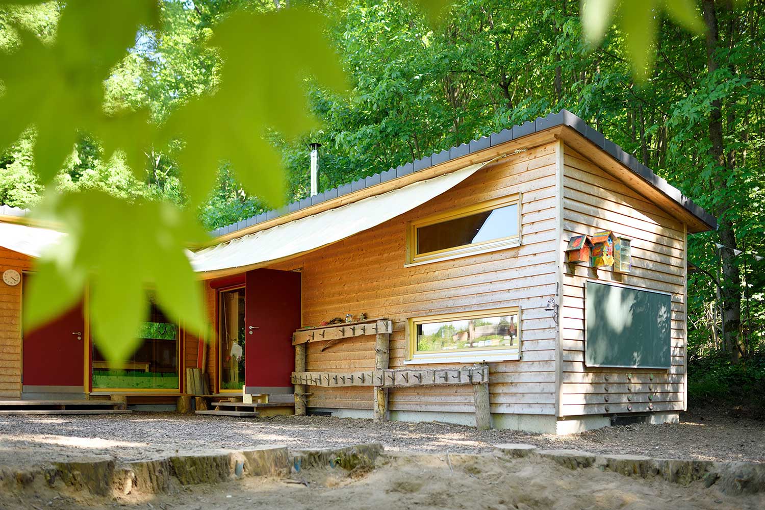 Holz-Sandkasten des Waldkindergarten, im Hintergrund ist das Gebäude mit Tafel und Kleiderhaken zusehen